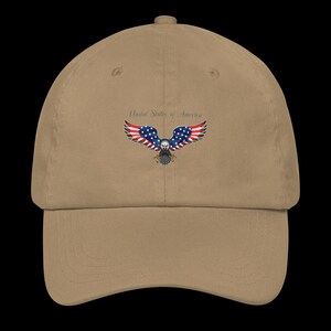 Puede incluir: Gorra de b&eacute;isbol beige con un dise&ntilde;o bordado de un &aacute;guila con los colores de la bandera estadounidense. El texto "United States of America" est&aacute; arqueado sobre el &aacute;guila.