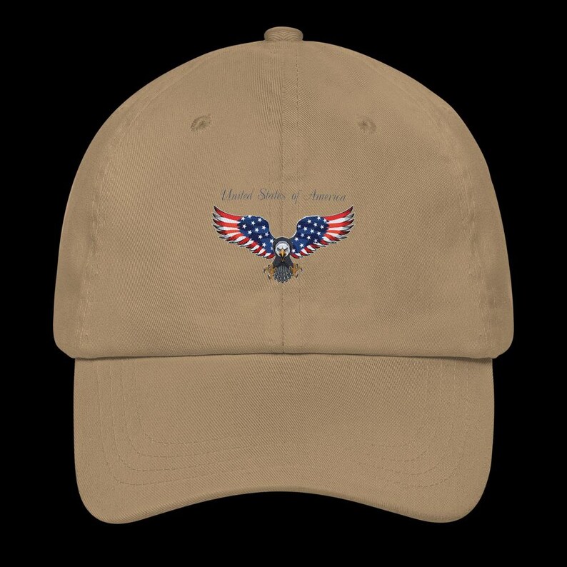 Puede incluir: Gorra de b&eacute;isbol beige con un dise&ntilde;o bordado de un &aacute;guila con los colores de la bandera estadounidense. El texto "United States of America" est&aacute; arqueado sobre el &aacute;guila.