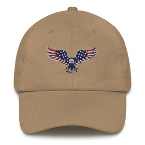 May include: A tan baseball cap with an embroidered design of an eagle with the American flag. The eagle's wings are red and white striped, and its body is blue with white stars. The cap has a curved peak and a fabric strap.