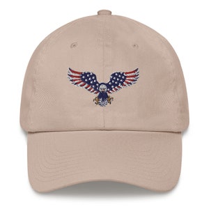 May include: A beige baseball cap with an embroidered eagle design. The eagle's wings are decorated with the stars and stripes of the American flag in red, white, and blue. The cap has a curved peak and an adjustable strap at the back.