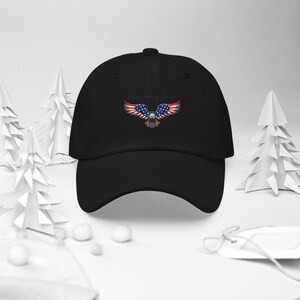 Puede incluir: Gorra de b&eacute;isbol negra con un dise&ntilde;o bordado de un &aacute;guila con alas con los colores de la bandera estadounidense. El texto "United States of America" est&aacute; arqueado sobre el &aacute;guila. La gorra tiene una visera curva y una correa ajustable.