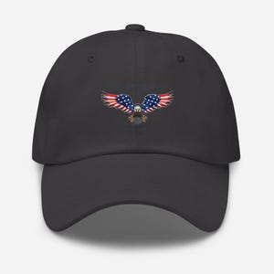 Puede incluir: Gorra de b&eacute;isbol gris oscuro con un dise&ntilde;o de &aacute;guila de la bandera estadounidense. Las alas del &aacute;guila son de rayas rojas y blancas, con estrellas azules. El cuerpo del &aacute;guila est&aacute; detallado con plumas marrones y blancas.