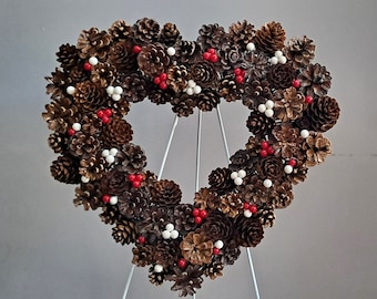 May include: A heart-shaped wreath made of pine cones, decorated with red and white berries.