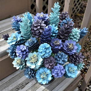 May include: A bouquet of blue and gray pine cones arranged in a vase. The pine cones are painted in shades of blue, teal, and gray, and they are arranged in a variety of sizes and shapes.