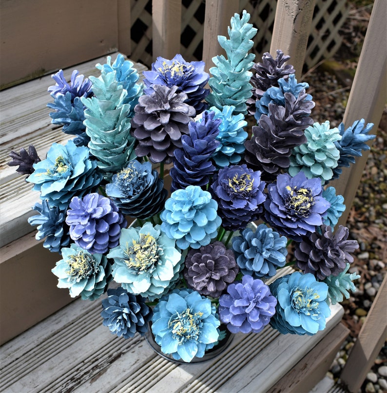 May include: A bouquet of blue and gray pine cones arranged in a vase. The pine cones are painted in shades of blue, teal, and gray, and they are arranged in a variety of sizes and shapes.