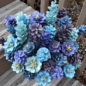 May include: A bouquet of pine cones painted in shades of blue, teal, and gray. The pine cones are arranged in a vase and look like a flower arrangement.