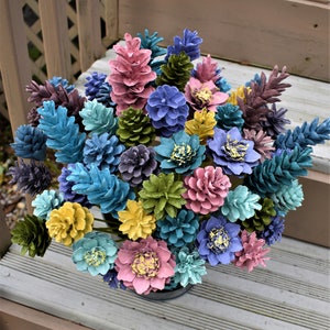 May include: A bouquet of painted pine cones arranged in a vase. The pine cones are painted in various colours, including blue, green, yellow, pink, and purple.