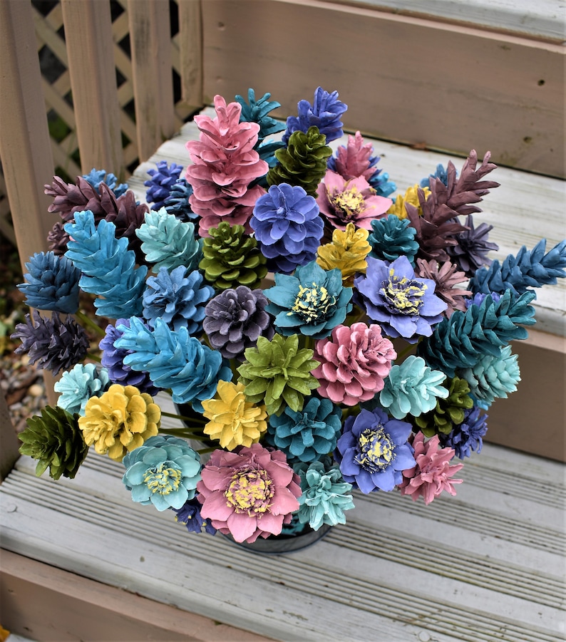 May include: A bouquet of painted pine cones arranged in a vase. The pine cones are painted in various colours, including blue, green, yellow, pink, and purple.