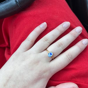 Może przedstawiać: Złoty pierścionek z owalnym, niebiesko-białym kamieniem. Kamień ma kwiatowy wzór.