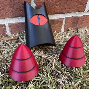 May include: Three 3D printed objects: a black figure with a red eye, and two red cone-shaped objects with black stripes.