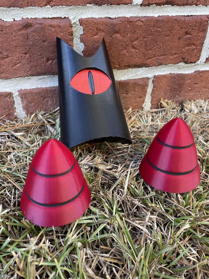 May include: Three 3D printed objects: a black figure with a red eye, and two red cone-shaped objects with black stripes.