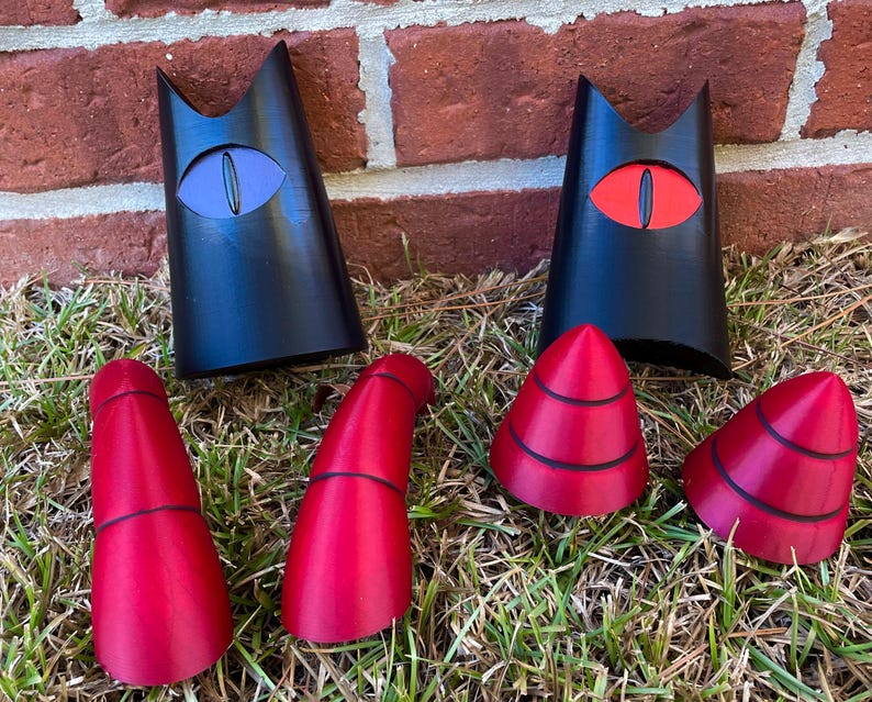 May include: A set of black and red cat-themed costume pieces. The set includes two black cat ears with red eyes, two red cat ears with black eyes, and two red pointy horns.