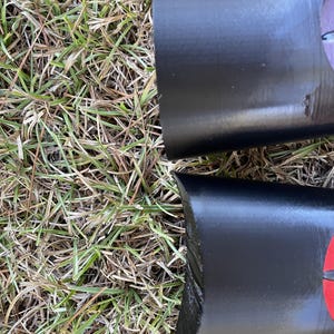 May include: Close-up of two black, cylindrical objects with red accents. The objects are lying on a bed of green grass.