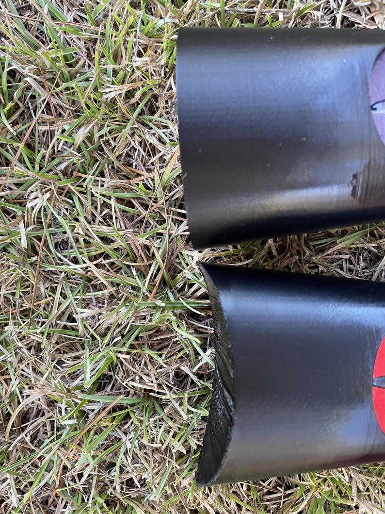 May include: Close-up of two black, cylindrical objects with red accents. The objects are lying on a bed of green grass.