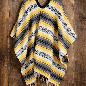 May include: A woven poncho featuring a striped pattern in yellow, charcoal gray, and white. The garment has a black V-neck collar and a fringed hemline. The fabric displays a repeating geometric motif integrated into the horizontal stripes.