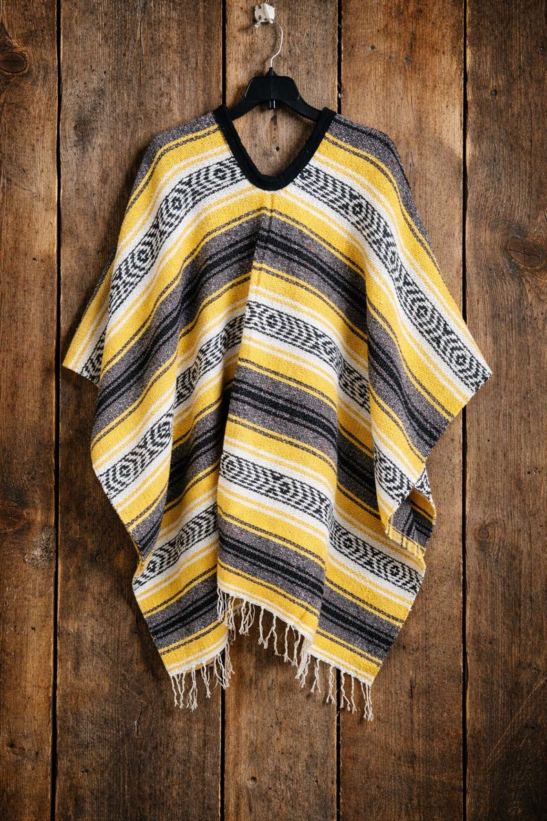 May include: A woven poncho featuring a striped pattern in yellow, charcoal gray, and white. The garment has a black V-neck collar and a fringed hemline. The fabric displays a repeating geometric motif integrated into the horizontal stripes.