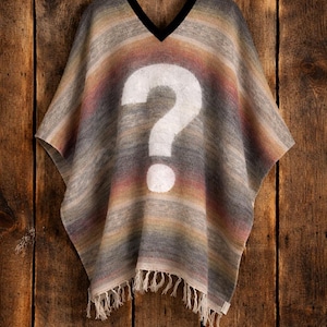 May include: A V-neck poncho featuring a horizontal gradient of muted earth tones including grey, tan, and soft pink. A large, white question mark is printed in the center of the garment. The hem is finished with a fringe of loose, off-white threads.