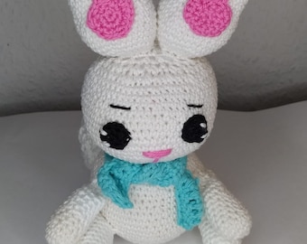 Peut inclure: Un lapin en crochet blanc avec des oreilles roses et une écharpe turquoise. Le lapin a des yeux noirs et un nez rose.