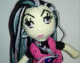 Peut inclure: Poupée en crochet avec de longs cheveux noirs, bleu sarcelle et blancs. La poupée porte une tenue en crochet rose et noire avec un bouton bleu.