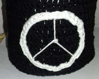 Peut inclure: Un récipient cylindrique en crochet noir avec un symbole de paix blanc brodé sur le devant.