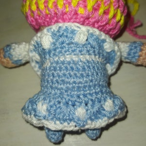 Pode incluir: Uma boneca de croch&ecirc; vestindo um vestido azul com bolinhas brancas e um chap&eacute;u rosa e amarelo.