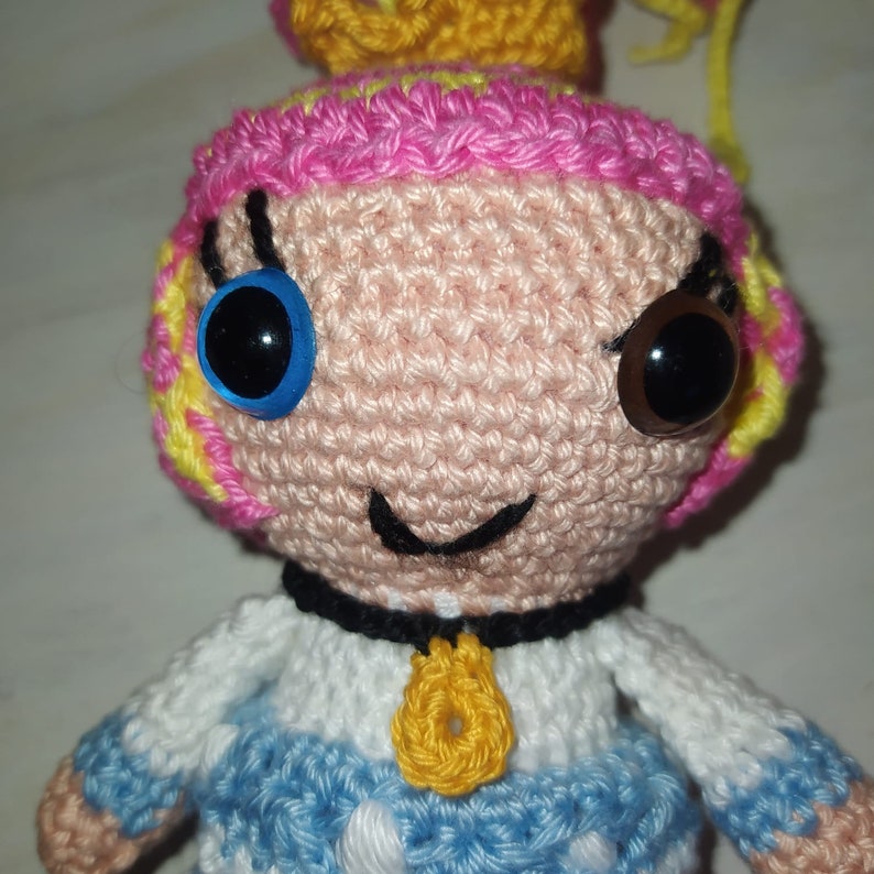 Pode incluir: Uma boneca de croch&ecirc; feita com fio rosa, amarelo e branco. A boneca tem olhos azuis e castanhos, uma boca preta e um pingente amarelo.