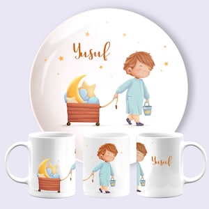 Op de afbeelding: Een set witte keramische mokken en een bord met een grillige illustratie. Het ontwerp toont een kind in een blauw outfit, een maan, sterren en de naam "Yusuf" in gouden letters. Het bord is rond, de mokken zijn cilindrisch.