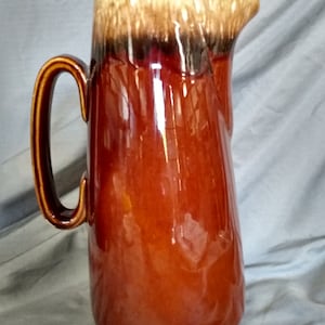 May include: A brown glazed ceramic coffee pot with a lid and a handle. The pot has a brown, black, and white glaze.