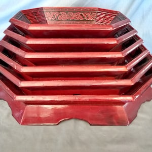 May include: A set of five red octagonal wooden serving trays with intricate carved designs. The trays are stacked on top of each other, creating a tiered display.