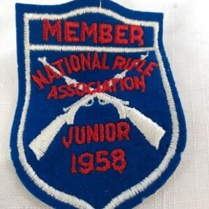 Può includere: Toppa ricamata blu e bianca con il testo "Member National Rifle Association Junior 1958". La toppa presenta due fucili incrociati.