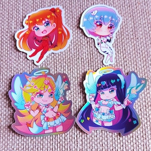 Peut inclure: Quatre autocollants colorés de style anime. Les autocollants présentent des personnages chibi avec de grands yeux et des cheveux vibrants. Deux autocollants ont des ailes d'ange. Les autocollants ont une finition holographique et sont sur une surface texturée.