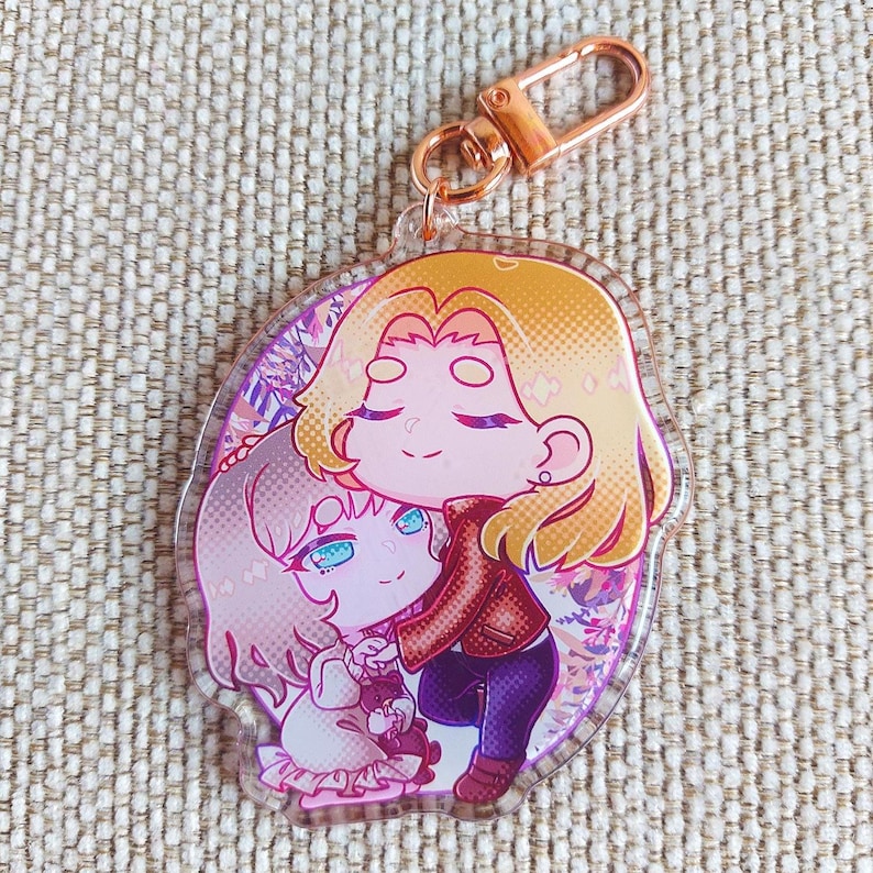 K&ouml;nnte beinhalten: Ein durchsichtiger Acryl-Schl&uuml;sselanh&auml;nger mit einer farbenfrohen Anime-Illustration von zwei sich umarmenden Figuren. Eine Figur hat blondes Haar und eine rote Jacke, die andere helles Haar und ein wei&szlig;es Outfit. Mit einem ros&eacute;goldenen Karabinerhaken.