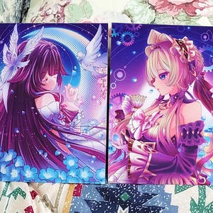 K&ouml;nnte beinhalten: Zwei rechteckige Kunstdrucke mit Charakteren im Anime-Stil. Der linke Druck zeigt eine Figur mit langem dunklen Haar, wei&szlig;en Fl&uuml;geln und blauen Blumen. Der rechte Druck zeigt eine blonde Figur in einem R&uuml;schenoutfit mit einer Teetasse.