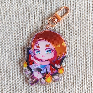 K&ouml;nnte beinhalten: Ein Schl&uuml;sselanh&auml;nger aus klarem Acryl mit einer Chibi-Figur mit kurzem braunem Haar, blauen Augen und einer kleinen Handfeuerwaffe. Die Figur ist von stilisierten gelben Flammen und einem dunklen, gezackten Hintergrund umgeben.