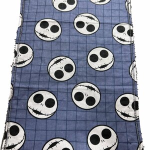 May include: A blue cloth featuring a grid pattern and repeated white Jack Skellington faces. The edges of the cloth are frayed. The Jack Skellington faces have black eyes and stitched smiles.