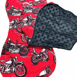 Könnte beinhalten: Eine rot-schwarze Wickelauflage mit Motorradaufdruck. Die Auflage hat ein Rautenmuster und zeigt Illustrationen von Motorrädern in Schwarz und Weiß. Ein separater, strukturierter, quadratischer schwarzer Pad ist angebracht.
