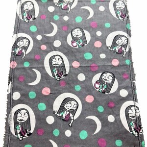 May include: Grey fabric featuring a repeating cartoon character design within white circles, interspersed with pink, teal, and white polka dots and crescent moons. The edges have a white stitched border.