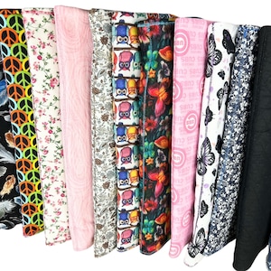 Puede incluir: Una colección de diversas telas estampadas, incluyendo diseños florales, de símbolos de la paz, búhos y mariposas. Los colores van del rosa y blanco al negro y azul. Algunas telas presentan el texto "CUBS".