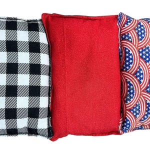 May include: Three decorative throw pillows. One pillow features a black and white buffalo check pattern. The center pillow is solid red. The third pillow has a patriotic design with red, white, and blue stars and stripes.
