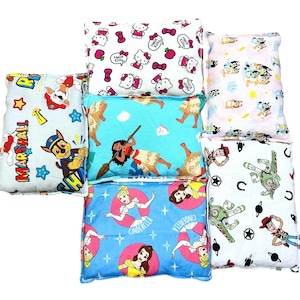 Può includere: Una collezione di piccoli cuscini quadrati con varie stampe di personaggi dei cartoni animati. I disegni includono Hello Kitty, principesse Disney, Paw Patrol e personaggi di Toy Story. I cuscini sono in tonalità di blu, rosa e bianco.