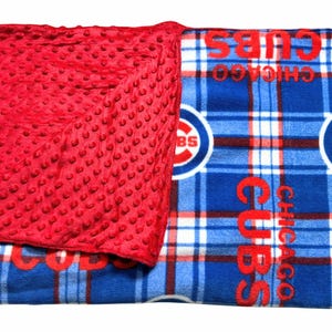 May include: A red, textured blanket with a blue and white plaid pattern. The blanket features the Chicago Cubs logo and the word "CUBS" in red. The blanket is a cozy and comfortable item.