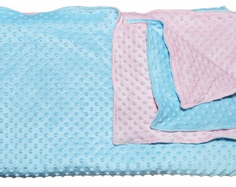 May include: A baby blanket in soft, textured fabric. The blanket is primarily light blue, with a pink section folded over. The fabric has a dimpled, raised dot pattern. The blanket is rectangular.