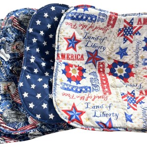 May include: A stack of four patriotic-themed fabric items. The items feature red, white, and blue patterns with stars, stripes, and text that reads "America," "Land of Liberty," and "Independence." One item has a navy blue background with white stars.