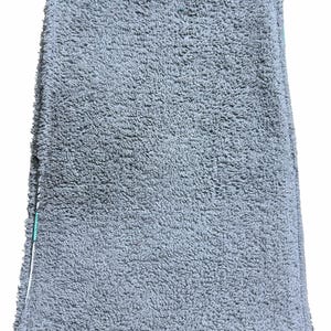 May include: A folded, grey, plush towel with a textured surface. The towel has a soft, absorbent appearance, suggesting it is made of a high-quality material. The edges are neatly finished, and a white and green accent is visible.