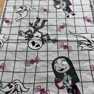 May include: White fabric with a black grid pattern, featuring characters from The Nightmare Before Christmas. The design includes Jack Skellington, Sally, Zero, and purple spiders. Suitable for crafting or decorative purposes.