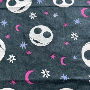 May include: Dark teal fabric with a repeating pattern of white skull faces, stars, and crescent moons. The stars are white, the moons are magenta, and the smaller stars are lavender. The skull faces have stitched mouths.