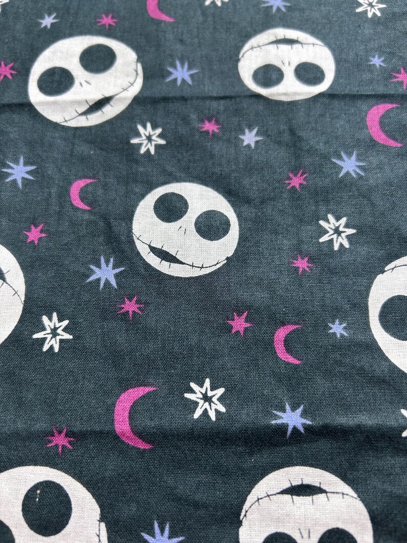 May include: Dark teal fabric with a repeating pattern of white skull faces, stars, and crescent moons. The stars are white, the moons are magenta, and the smaller stars are lavender. The skull faces have stitched mouths.