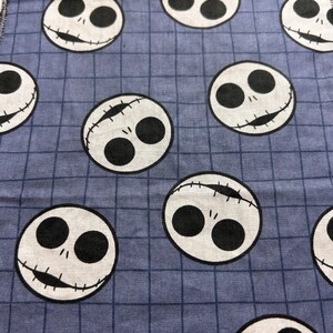 May include: Close-up of a blue fabric with a grid pattern. The fabric is covered with white circles featuring black eyes and stitched mouths, resembling a character from a popular animated film. The design is repeated across the fabric.
