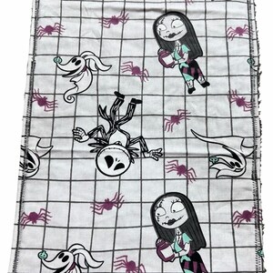 May include: White fabric with a black grid pattern featuring cartoon characters from The Nightmare Before Christmas. The design includes Jack Skellington, Sally, Zero, and purple spiders. The edges are finished with a black zigzag stitch.