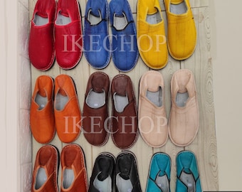 May include: A variety of leather slippers in different colors, including red, orange, brown, blue, yellow, and turquoise. The slippers are arranged in three rows of four pairs each. The slippers are all made of leather and have a simple design.